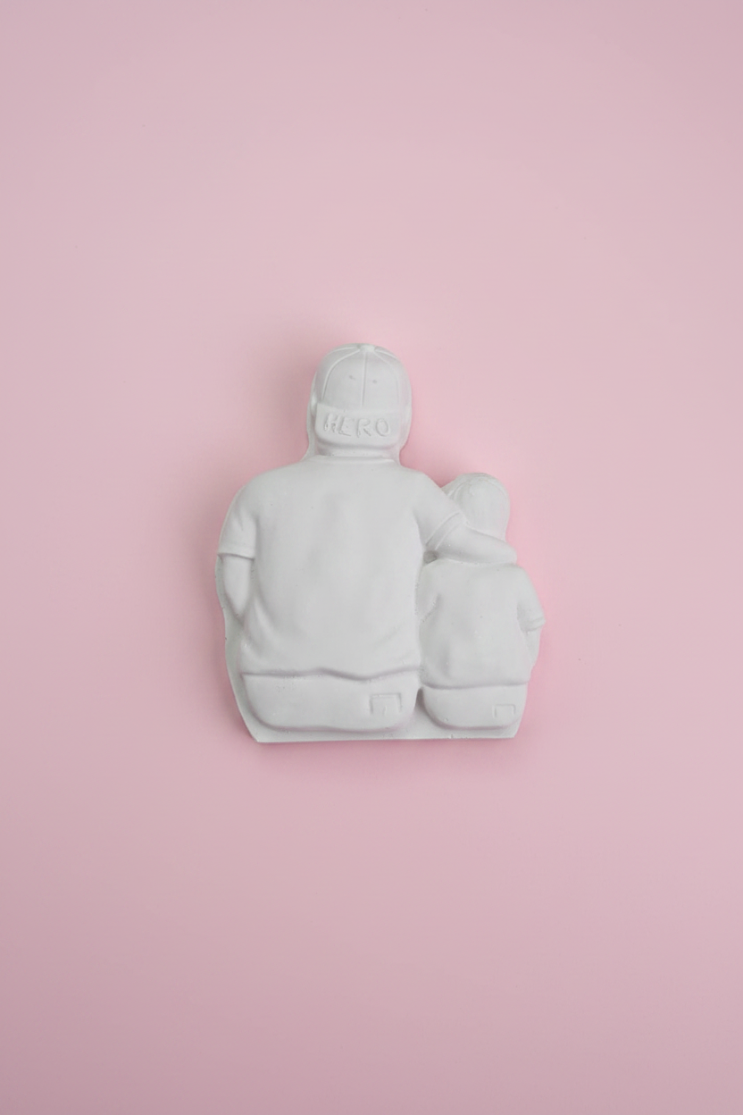 White unpainted plaster Hero Dad and child relief figure on pastel pink surface