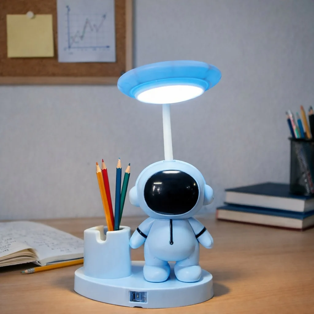 Blue astronaut LED desk lamp with pen holder glowing on a study desk with pencils and books