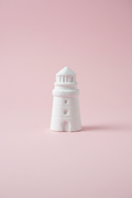 White unpainted plaster lighthouse figure on pastel pink surface